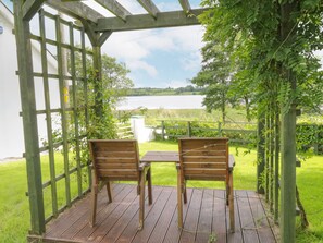 Une terrasse en bois avec deux chaises et une table, donnant sur un lac.