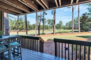 Un espacio al aire libre cubierto con una terraza de madera, una mesa y sillas, y vistas a un campo de golf.