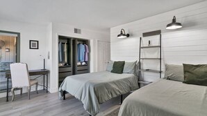 Habitación con dos camas, un escritorio y una silla. Se observa un armario con ropa y una escalera.