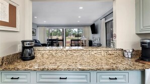 Una cocina con encimeras de granito, cafetera y vista a un patio exterior con mesa y sillas.