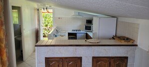 A kitchen with a tiled backsplash, a stove, a microwave, and a refrigerator. There is a window with a view of greenery outside.