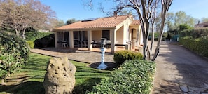 A house with a tiled roof, a patio with outdoor furniture, and a garden with a stone sculpture.