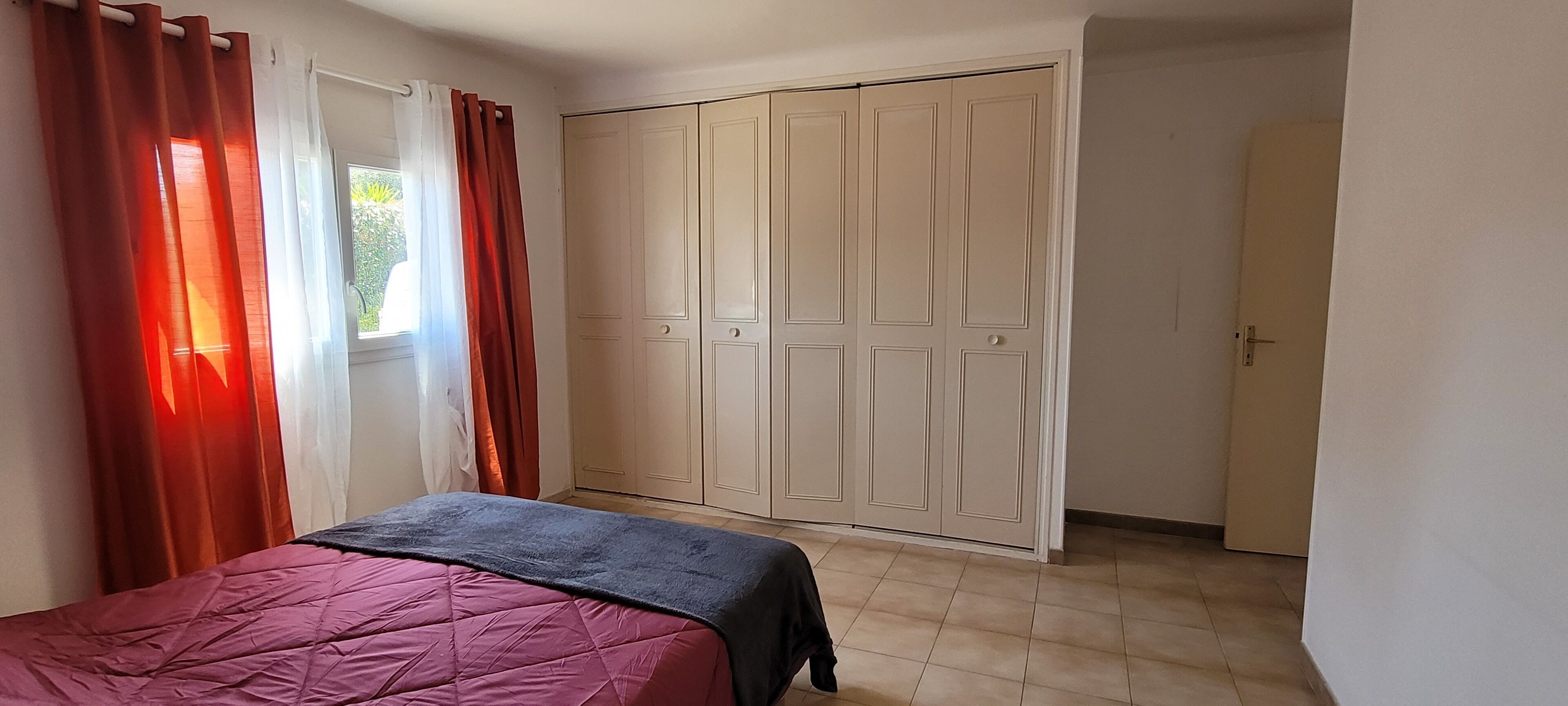 A bedroom with a bed, a wardrobe, and a window with curtains.