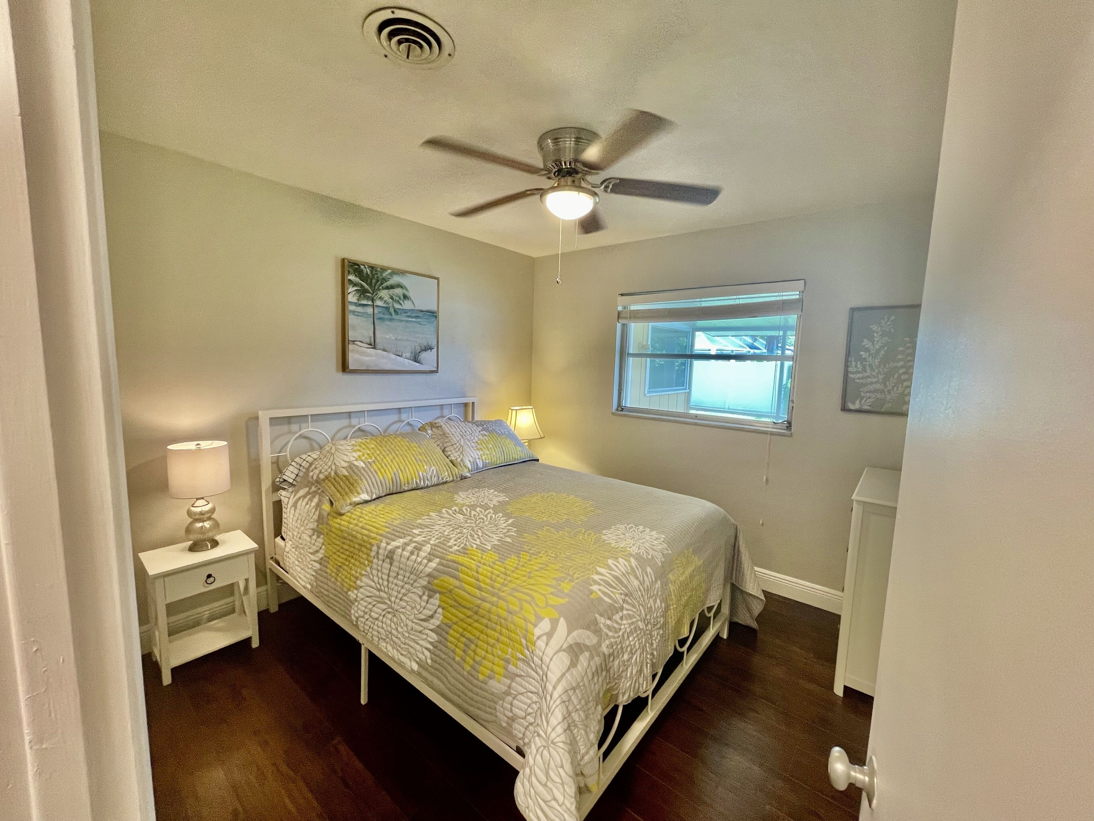 Une chambre à coucher avec un lit, un ventilateur de plafond, une fenêtre et une table de chevet avec une lampe.