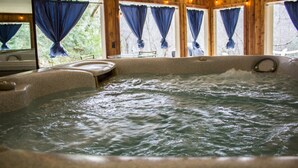 Un bain à remous avec un intérieur en bois, de nombreuses fenêtres ornées de rideaux bleus et une vue sur la verdure environnante.