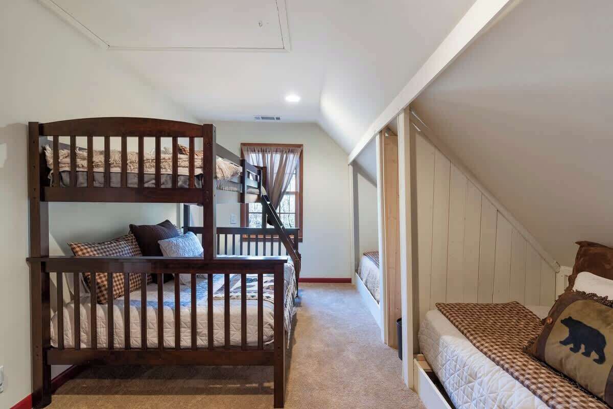A bedroom with a bunk bed, a single bed, and a staircase leading to an upper level.