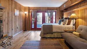 Une pièce aux murs lambrés, comprenant un lit, un canapé, une lampe et une vue sur l’extérieur par une porte.