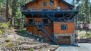 Une cabane en rondins à deux étages, dotée d’un balcon, de fondations en pierre et d’un garage.
