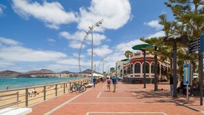 Ein promenadebelagter Weg mit einem Strand im Hintergrund, Bänken und Straßenlaternen.