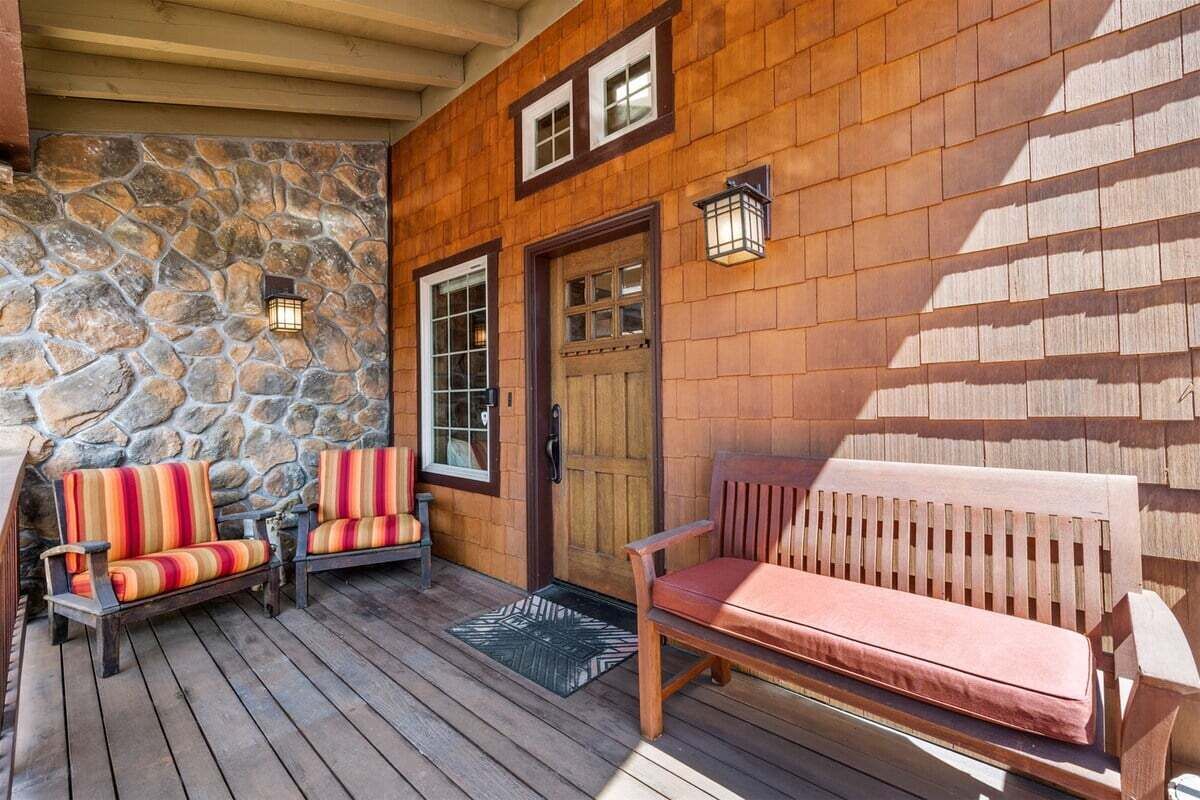 Une terrasse en bois avec un mur en pierre, une porte en bois et deux bancs dotés de coussins.