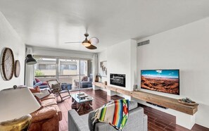A modern living room with a large flat-screen TV, leather sofas, a coffee table, and a ceiling fan.