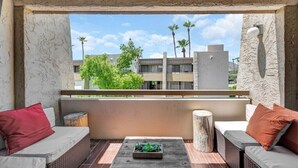 En balkon med udsigt til bygninger og palmer, møbleret med en sofa og et lille bord.