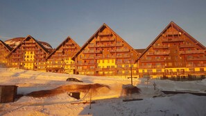 A row of wooden chalet-style buildings with balconies, set in a snowy landscape.