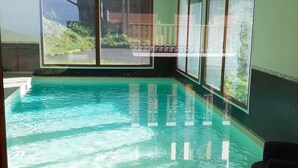 A modern indoor swimming pool with clear glass walls, a tiled floor, and a view of the outdoors. - Appart "les luges" 4/6 people valley view large balcony swimming pool  (Besse-et-Saint-Anastaise)