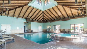 Ein Hallenbad mit hoher Holzbalkendecke, gefliestem Boden und Blick ins Freie durch große Fenster.