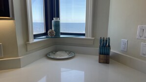 Eine Küche mit weißer Arbeitsplatte, einem Fenster mit Meerblick, einer dekorativen Vase und einem Messerblock.