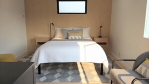 A modern bedroom with a large bed, two bedside tables, a small window, and a patterned rug. - Unwind in the sizeable comforts of this small modern space. (Bozeman)
