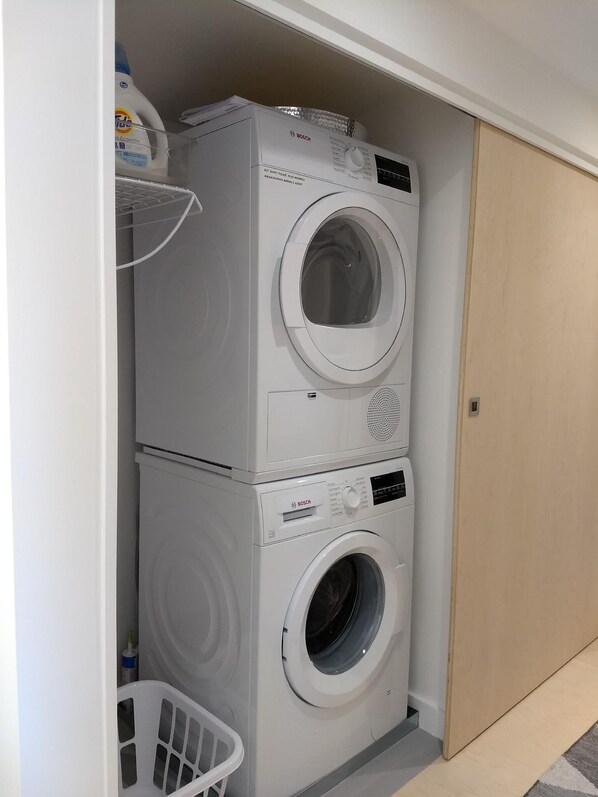 Un área de lavandería compacta con lavadoras apiladas y un tendedero.