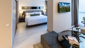 Moderni hotellihuone, jossa on suuri sänky, seinälle asennettu taulutelevisio ja ikkunasta avautuva näkymä ulos.