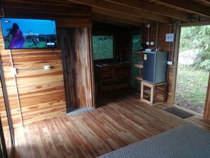 A wooden cabin interior with a television mounted on a wall, a small kitchen area, and a view of the outdoors. - 4 Luxury Cabins 5 stars. (Copacabana)