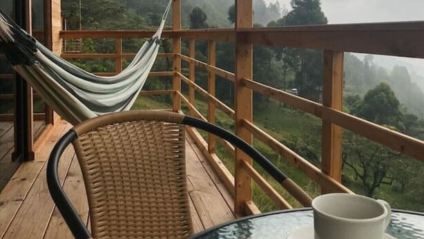Une terrasse en bois avec un fauteuil en osier et un hamac, offrant une vue sur un paysage montagneux.