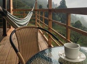 Une terrasse en bois avec un fauteuil en osier et un hamac, offrant une vue sur un paysage montagneux.
