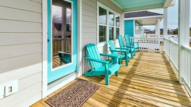 A porch with turquoise Adirondack chairs, a wooden deck, and a white railing.