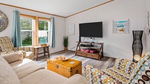 Un salon avec un canapé, une table basse, un téléviseur posé sur un meuble en bois et une fenêtre avec des rideaux.