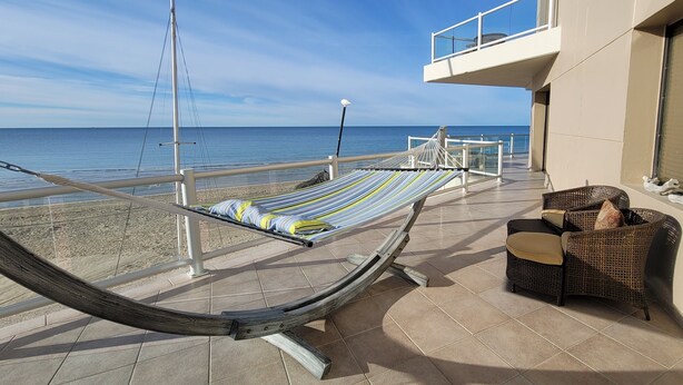 Un hamac sur un balcon donnant sur la mer, avec un fauteuil en osier et un sol carrelé.