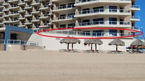 Un hôtel situé en bord de mer, doté de nombreux balcons, de chaises longues et de parasols en chaume.
