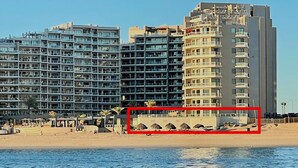 Un hôtel situé en bord de mer, avec plusieurs étages, des balcons et une plage de sable.