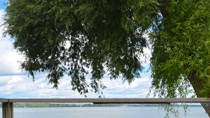 Una terraza de madera con dos sillas y una mesa, con vista a un lago tranquilo.