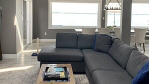 Una sala de estar moderna con un sofá seccional gris, una mesa de centro y grandes ventanales con vista al agua.