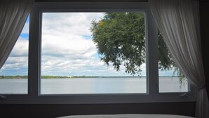 Un dormitorio con un ventanal que da a un lago y un árbol.
