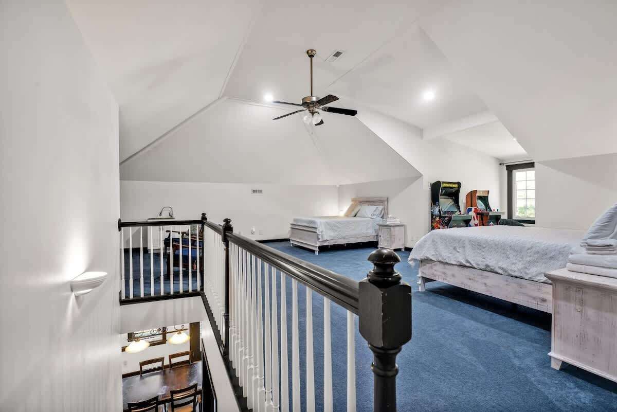 Une chambre avec un plafond en pente, un ventilateur de plafond, deux lits, un bureau et une chaise.