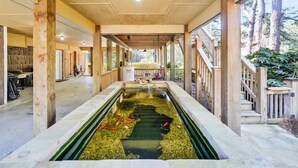 Une allée couverte agrémentée d’un élément aquatique central, de colonnes en bois et offrant une vue sur l’extérieur.