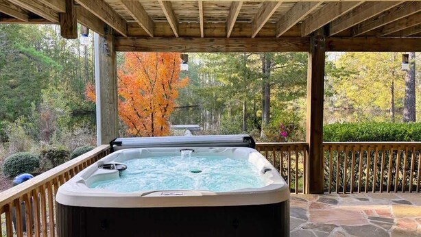 Un bain à remous sous une pergola en bois, avec une terrasse en pierre, le tout entouré du feuillage automnal.