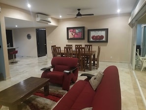 Un salon avec un canapé rouge, une table basse en bois et un coin repas comprenant une table et des chaises en bois.