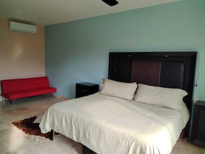 Une chambre à coucher avec un lit, un canapé rouge, une petite commode noire et un appareil de climatisation.