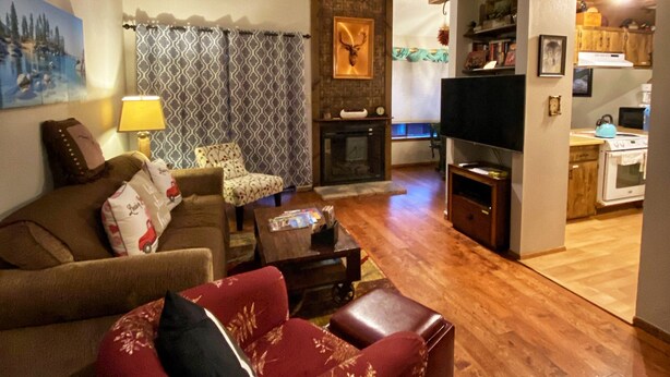 A living room with a fireplace, a television, and a kitchen area. - Walk To Ski Lifts! W/D, WiFi, Kitchen, Skylights (Angel Fire)