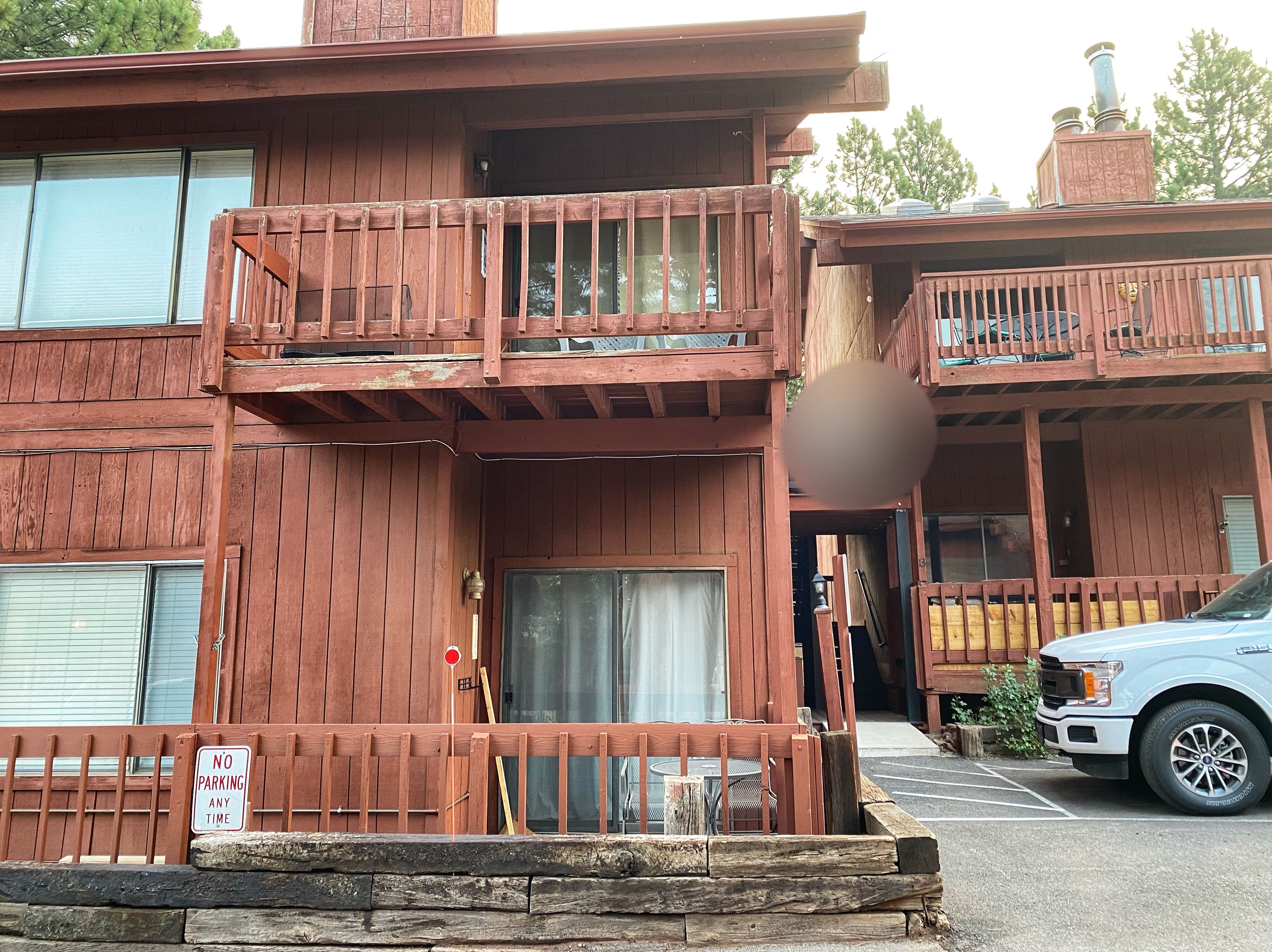 A two-story wooden building with balconies, a 'No Parking Any Time' sign, and a parked truck.