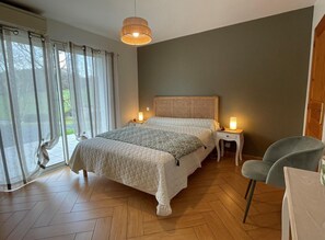 A bedroom with a large bed, two bedside tables, a chair, a hanging light fixture, and a view of the outdoors. - Jauregia - Saint-esteben (SAINT-ESTEBEN)