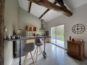A kitchen with a large island, two bar stools, a wooden cabinet, and a view through a glass door. - Jauregia - Saint-esteben (SAINT-ESTEBEN)