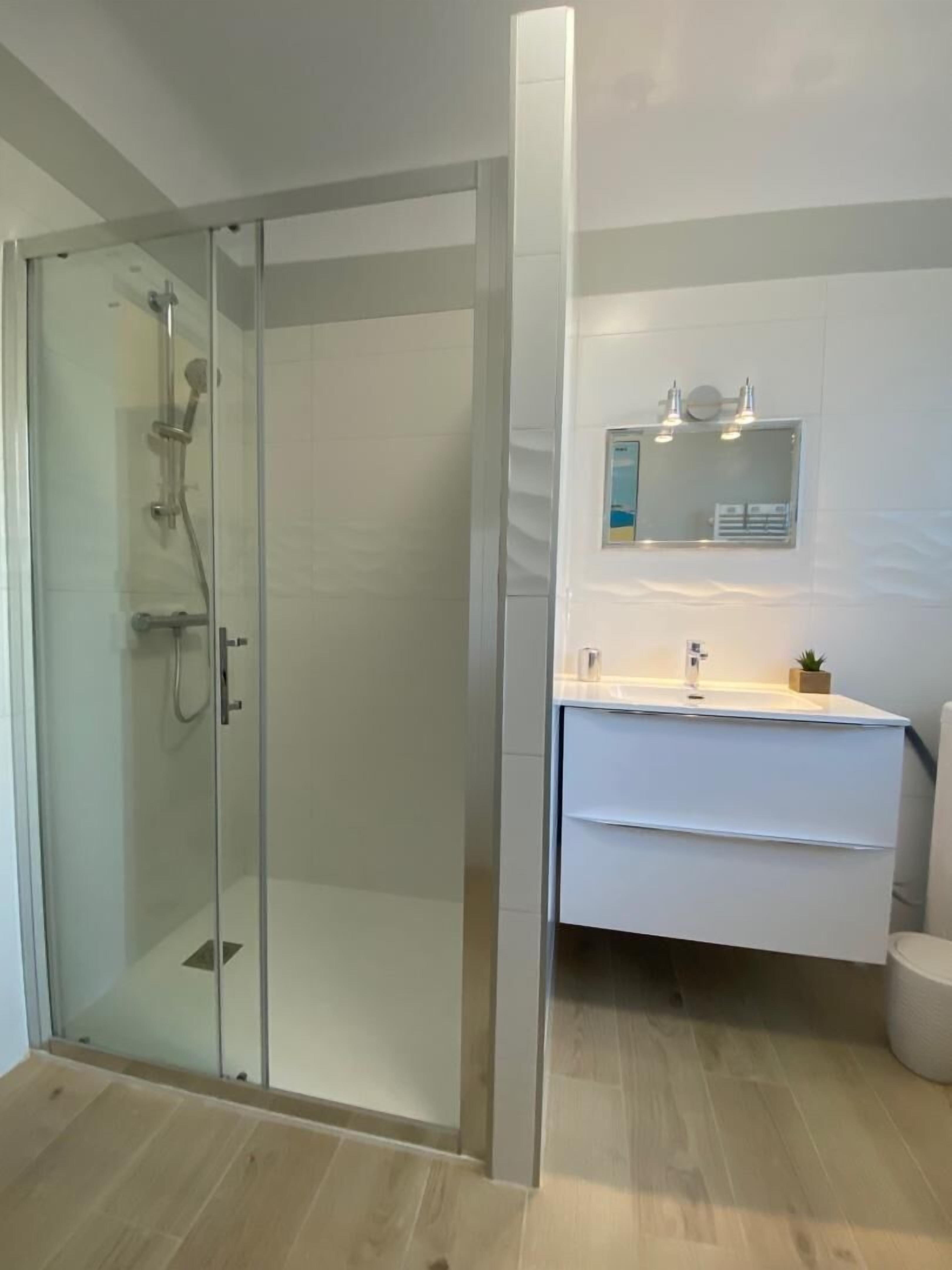A modern bathroom with a glass shower enclosure, a white vanity with a mirror, and a toilet.
