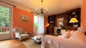 A cozy living room with a sofa, armchair, and a coffee table. There is a bookshelf, a mirror, and a chandelier. - Villa ANNE-MARIE - BAYONNE (BAYONNE)