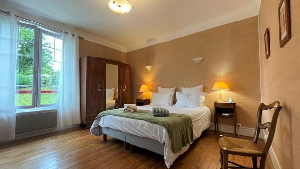 A hotel room with a bed, two bedside lamps, a chair, a wardrobe, and a view of greenery outside. - Villa ANNE-MARIE - BAYONNE (BAYONNE)