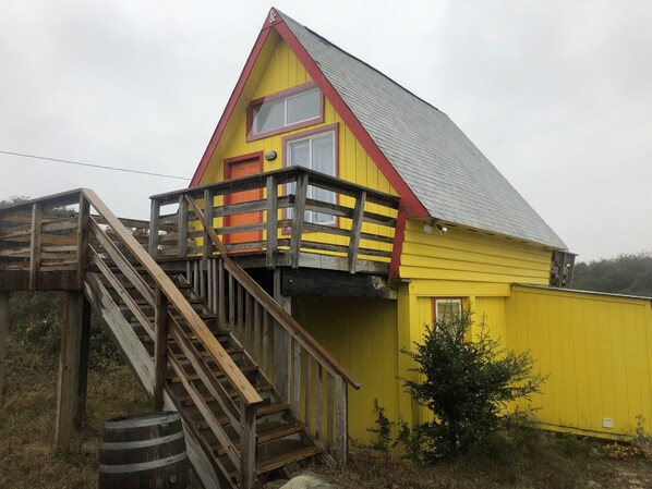A yellow house with a red roof and a wooden staircase leading to a balcony.
