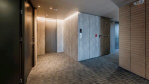 A modern hallway with a carpeted floor, wooden walls, and a door with a red emergency exit sign.