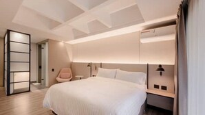 A modern hotel room with a large bed, a bedside table, a nightstand, and a built-in wardrobe.