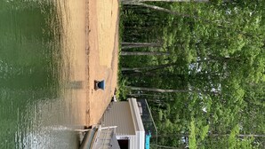 A boat docked at a sandy beach with a forested area in the background. - 2 Bedroom Camper with Rooftop Boat House Deck (Gwinn)